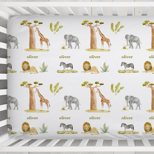 Close-up of Wildwood Safari crib sheet with watercolor giraffes, elephants, lions, zebras, and the name Oliver in olive green.