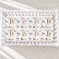 Overhead view of Wildwood Safari personalized crib sheet with safari animals, trees, greenery, and the name Oliver in a white crib.