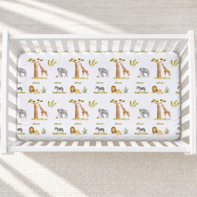 Overhead view of Wildwood Safari personalized crib sheet with safari animals, trees, greenery, and the name Oliver in a white crib.