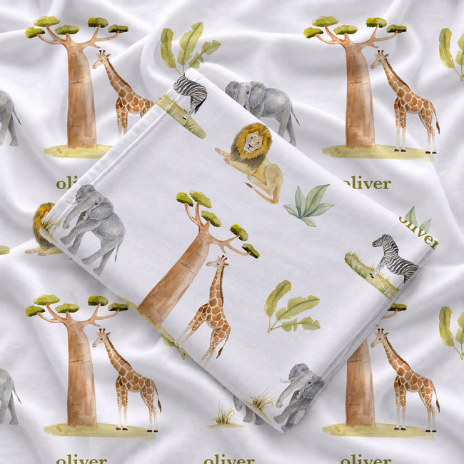 Folded Wildwood Safari personalized swaddle blanket showing watercolor safari animals, leafy greenery, and Oliver in olive green lettering.