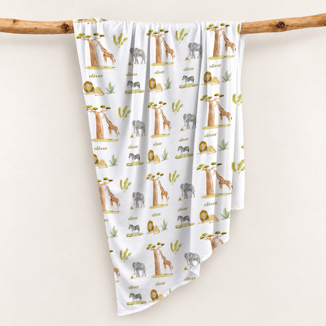 Wildwood Safari swaddle blanket personalized with Oliver, draped over a wooden branch to display the safari animal and tree pattern.
