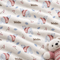A close-up of a soft fleece blanket with a winter-themed pattern featuring polar bears in pink sweaters, blue leaves, berries, and the word 'Winter' printed repeatedly. A plush teddy bear wearing a pink sweater is partially visible in the lower right corner.