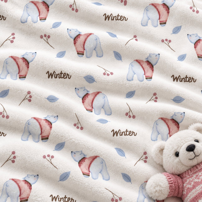 A close-up of a soft fleece blanket with a winter-themed pattern featuring polar bears in pink sweaters, blue leaves, berries, and the word 'Winter' printed repeatedly. A plush teddy bear wearing a pink sweater is partially visible in the lower right corner.