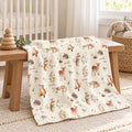 A cream-colored baby blanket with a woodland animal print featuring foxes, deer, hedgehogs, and acorns, draped over a wooden bench in a nursery setting.