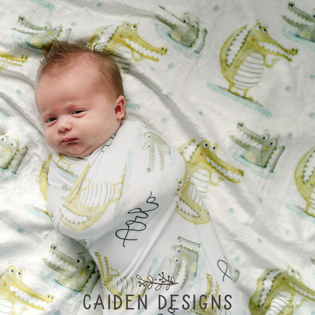 baby wrapped in gator swaddle and laying on a gator personalized baby blanket