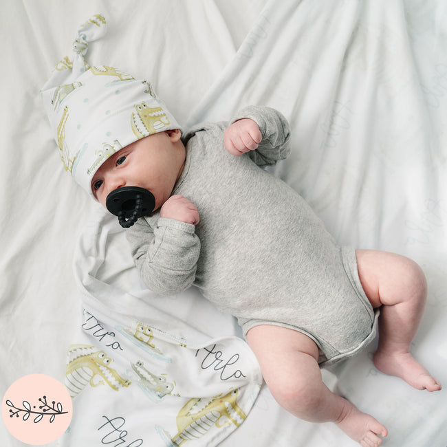 baby wearing a gator knotted baby hat and laying on a matching receiving blanket
