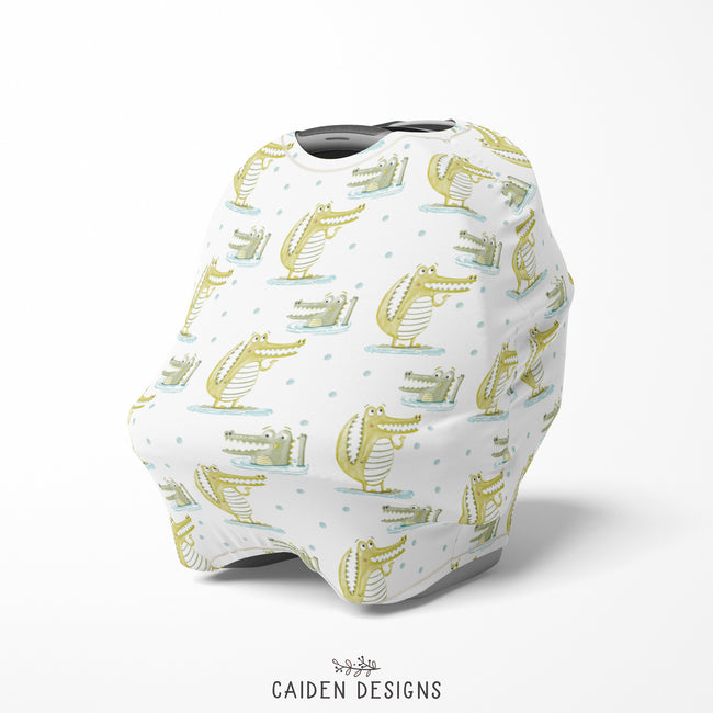 White baby car seat cover with green alligator patterns and a black tapered shape at the top, likely to be used as a nursing cover.