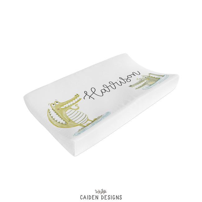 A white personalized changing pad cover with an alligator illustration and the name 'Gator' sewn on it.