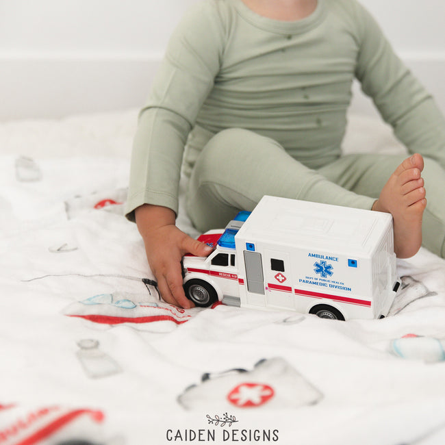 A child interacting with a white and red toy ambulance blanket, with the ambulance design printed on the blanket.