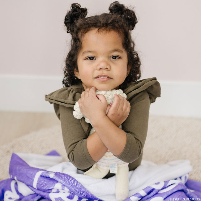 little girl with a toy and a purple personalized blanket