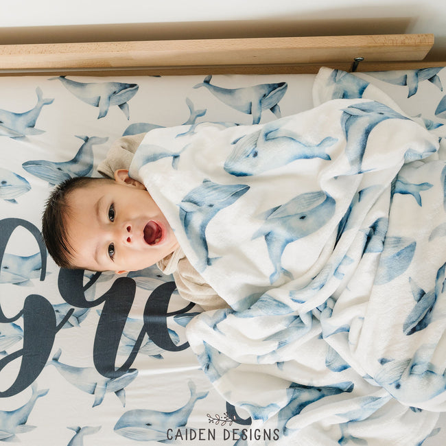 A child on a blue and white whales pattern personalized crib sheet with a matching baby blanket