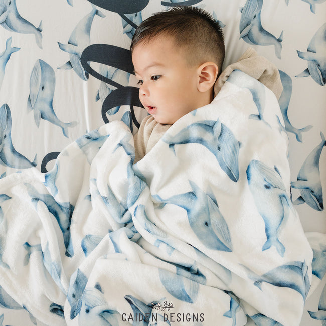 A child on a blue and white whales pattern crib sheet with a matching baby blanket