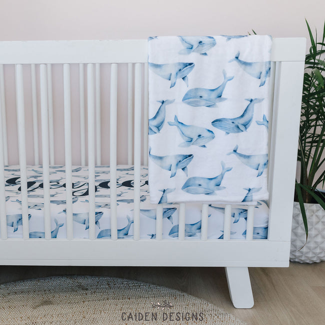 A blue and white whales pattern crib sheet with a matching baby blanket