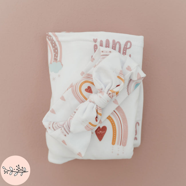 folded personalized baby swaddle and headband with a boho rainbow pattern and name June