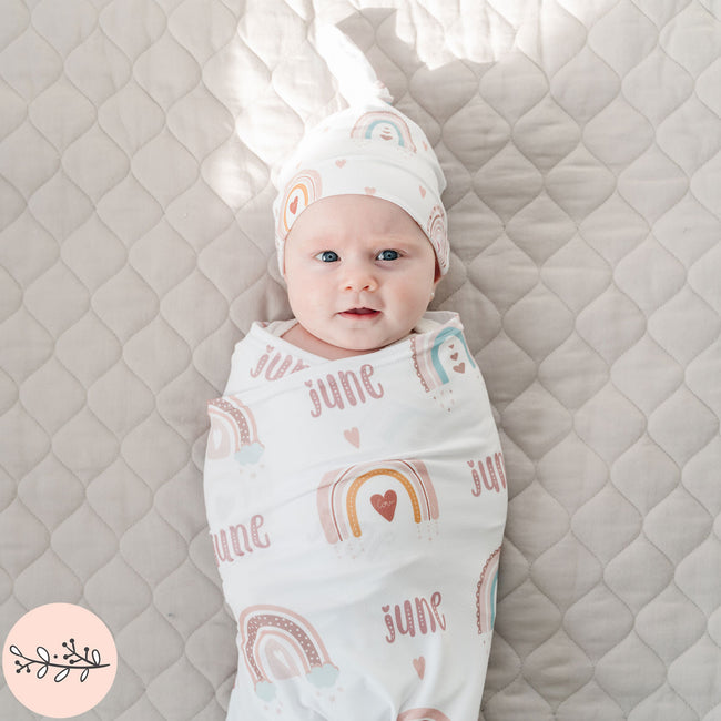 A baby wrapped in a personalized baby swaddle with a boho rainbow design