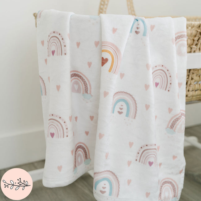 A personalized baby blanket with a boho rainbow design, displayed draped over a basket.
