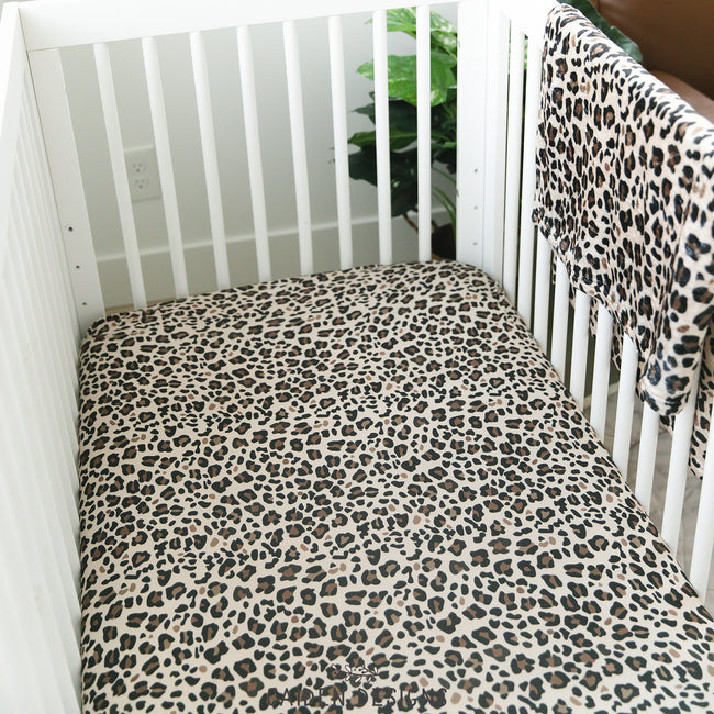 Brown leopard print crib sheet on a white crib with a matching baby blanket draped over the rail