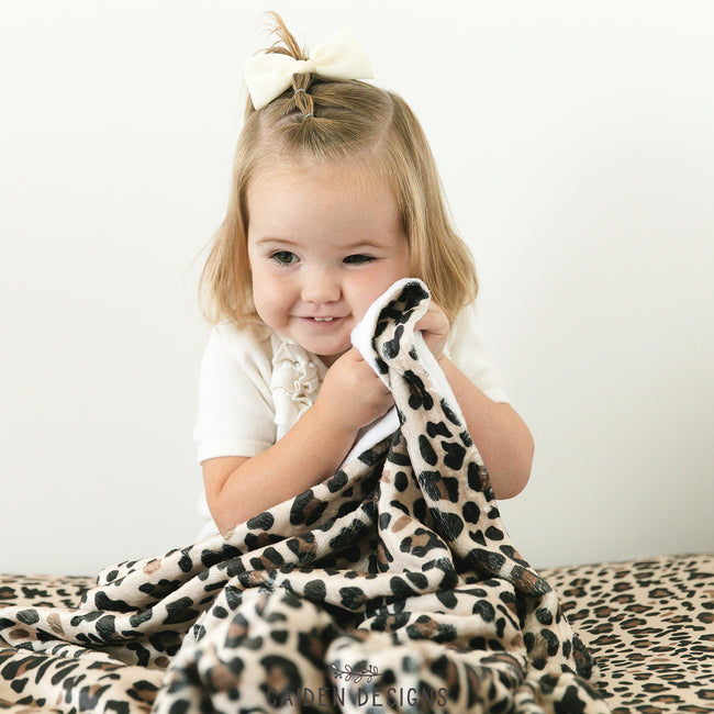 A child holding a brown leopard print custom throw blanket with a visible hand-sewn flat seam.