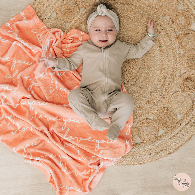 A baby laying on a peach personalized blanket with a white name printed on it.