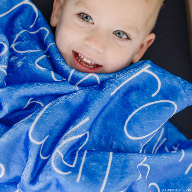 A child wrapped in a blue personalized blanket with a white name printed on it.