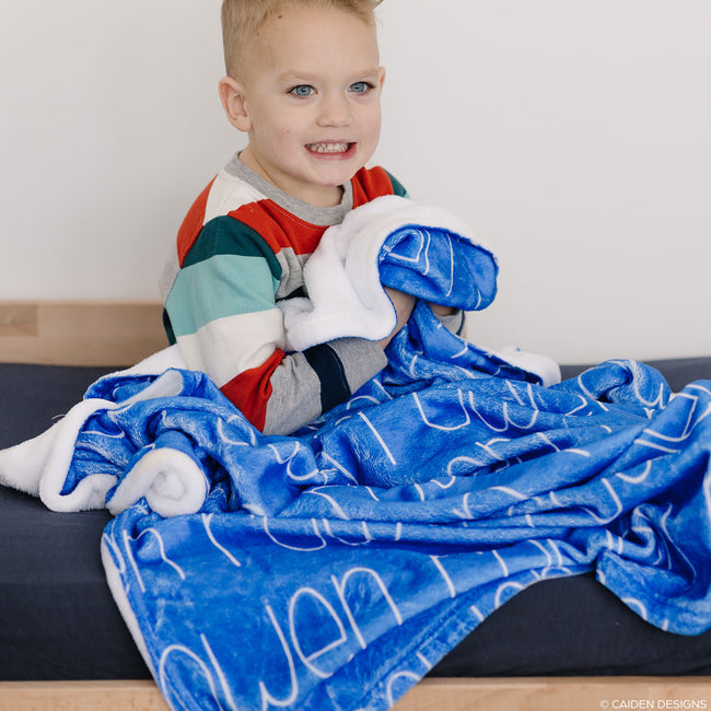 A child with a blue personalized blanket with a white name printed on it.