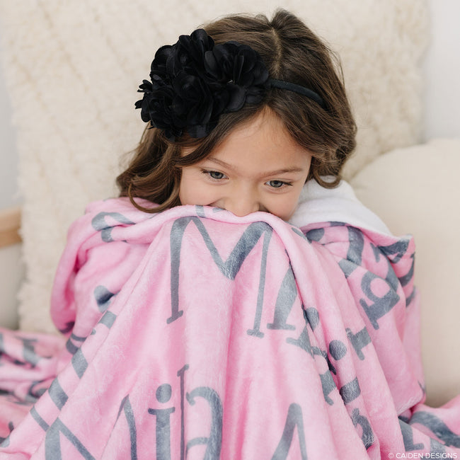 A child wrapped in a pink personalized blanket with the name 'Mila' printed on it.