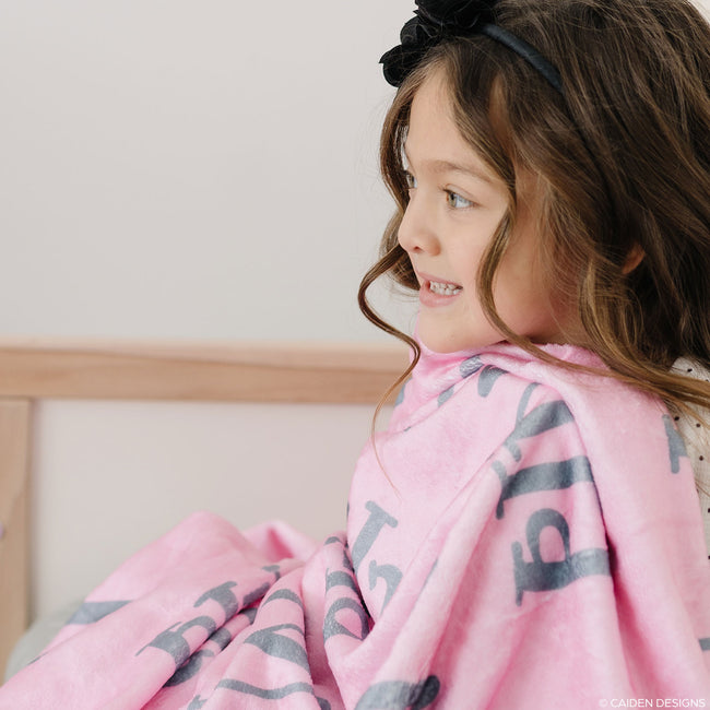 A child wrapped in a pink personalized blanket with the name 'Mila' printed on it.
