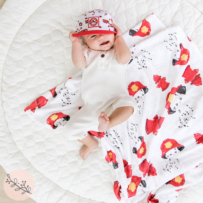 A baby lying on a personalized blanket with Dalmatian firehouse theme, including images of Dalmatians, fire hydrants, and fire engines.