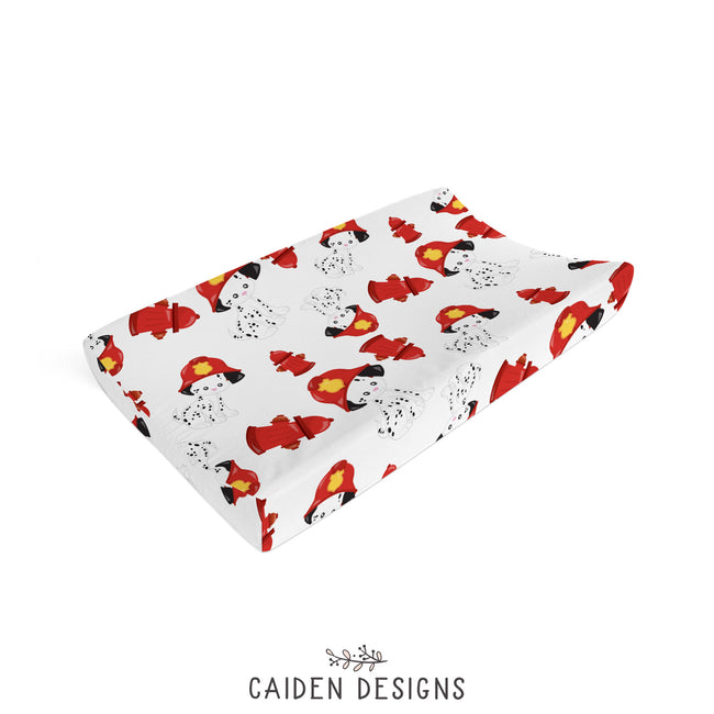 A changing pad cover featuring a white background with a repeating pattern of Dalmatian puppies in firefighter gear.