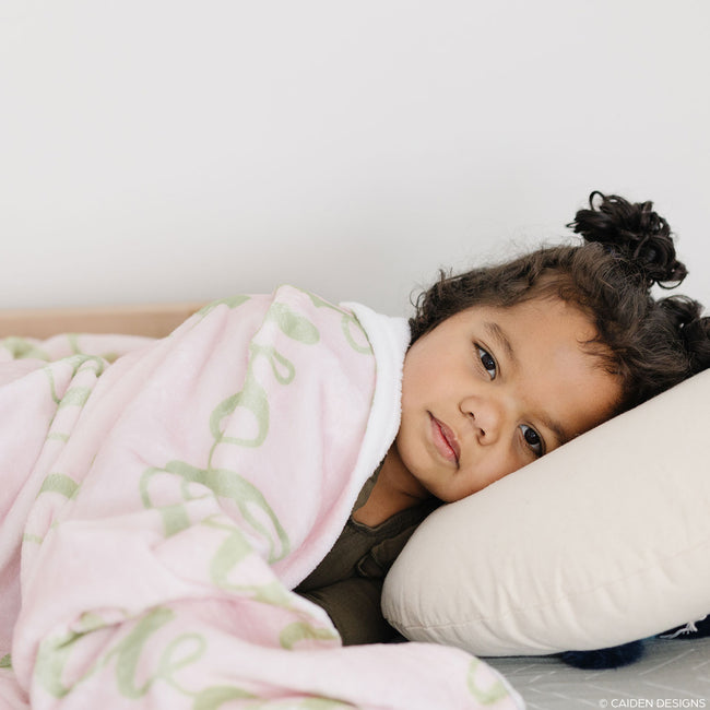 A child resting under a pink personalized blanket with green names on it.