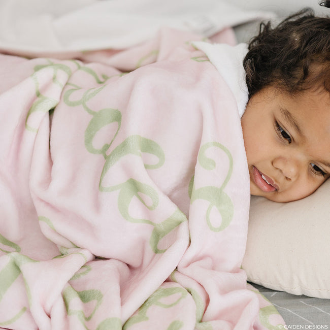 A child resting under a pink personalized blanket with green names on it.