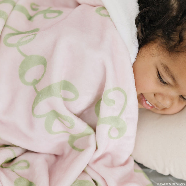 A child resting under a pink personalized blanket with green names on it.