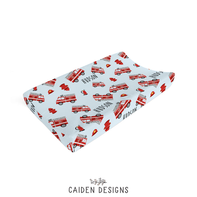 A personalized changing pad cover with a pattern of red fire trucks on a blue background