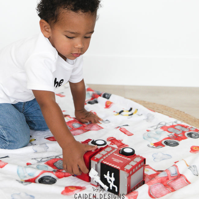 A young child playing with a toy on a personalized blanket featuring firefighting themes and characters.