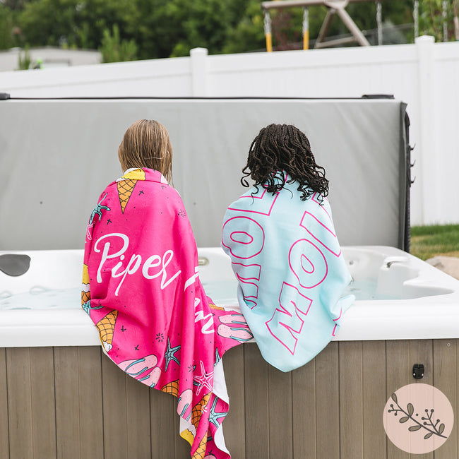 Two little girls sitting outside a jacuzzi with personalized beach towels