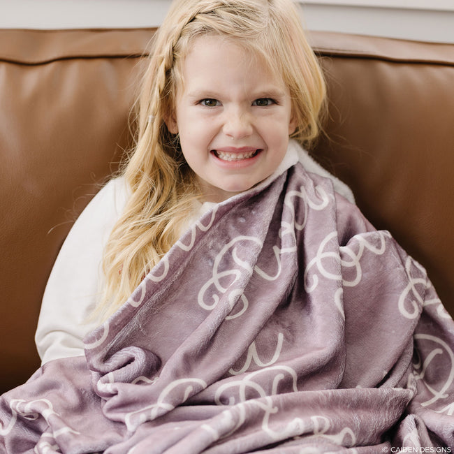 Girl with a mauve personalized baby blanket on a leather sofa