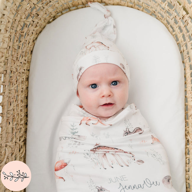 A baby swaddled in a blanket with woodland animal prints, lying in a wicker basket.