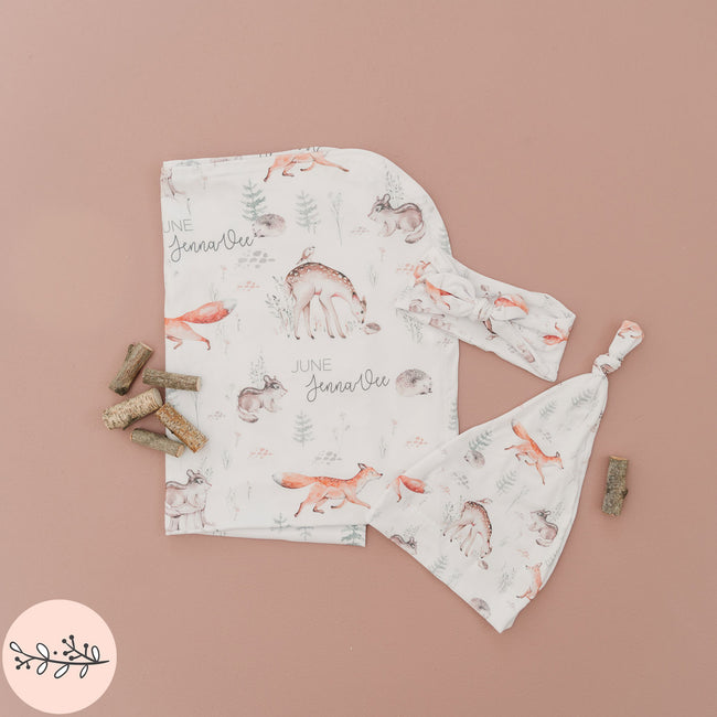 A personalized swaddle blanket, baby headband and hat featuring a woodland animal prints