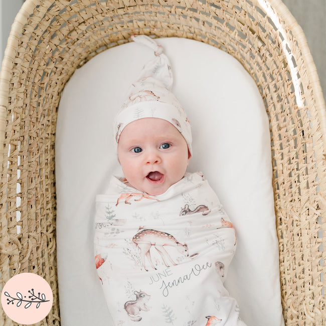A baby swaddled in a blanket with woodland animal prints, lying in a wicker basket.