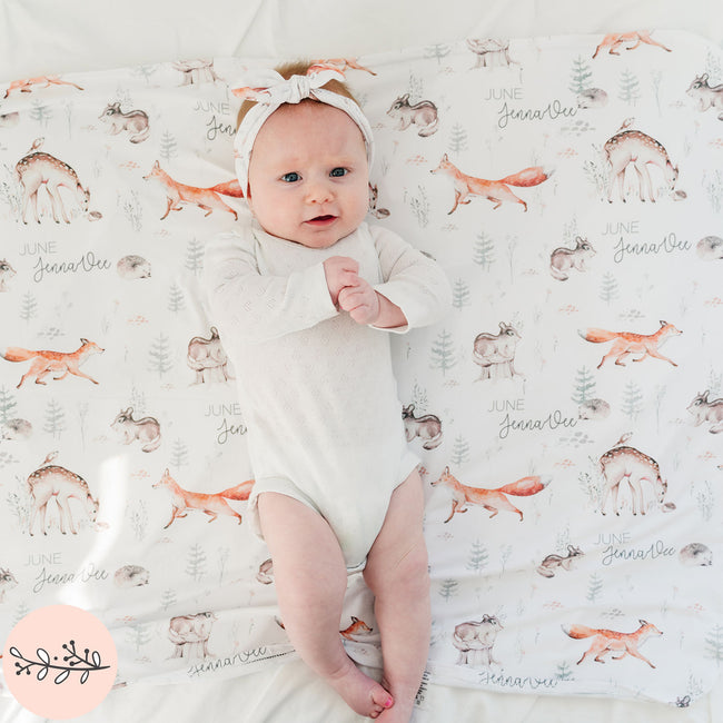 a baby girl laying on a personalized baby blanket with a pattern of woodland animals 