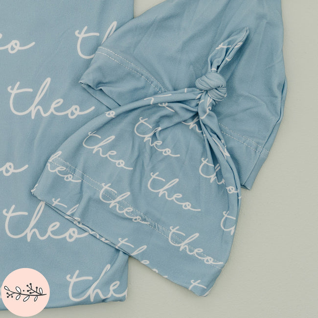 A beautiful set of personalized baby swaddle and hat. Featuring a handwritten font design with the name Theo as well as solid blue baby hat