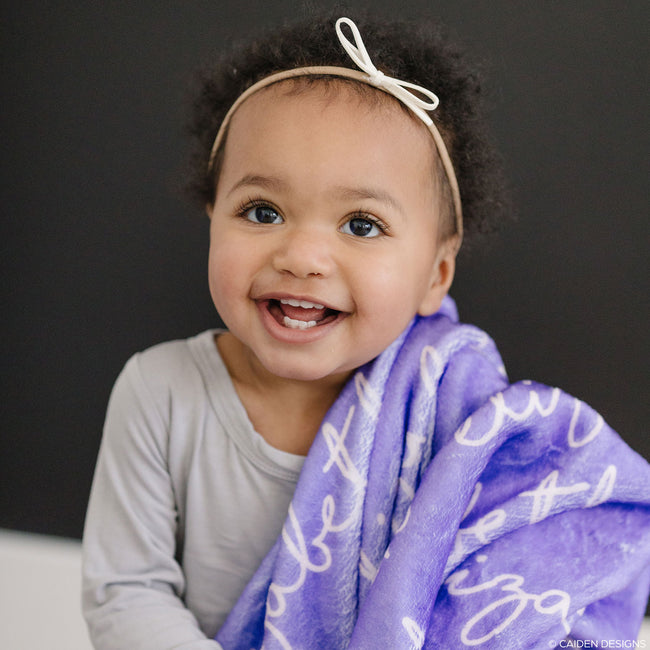 A child with a lilac personalized blanket with a name printed on it.