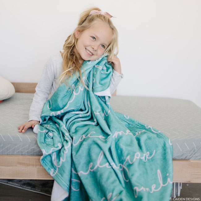A child with a teal personalized blanket with the name 'Amelia' printed on it.