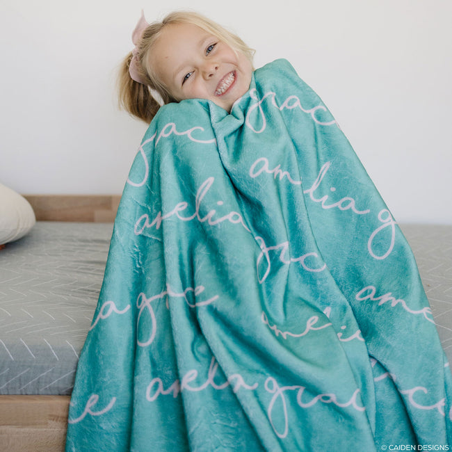 A child wrapped in a teal personalized blanket with the name 'Amelia' printed on it.