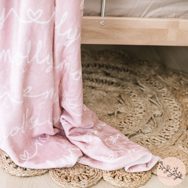 A dusty rose personalized blanket featuring a heart interlaced with the names