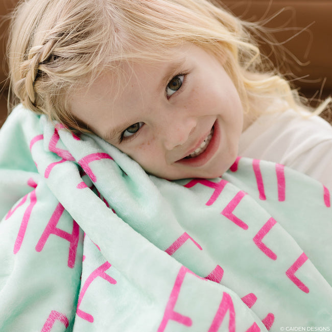 A girl with bright mint personalized blanket with hot pink letters