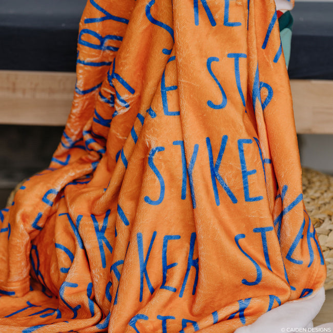 An orange personalized blanket with cobalt blue letters