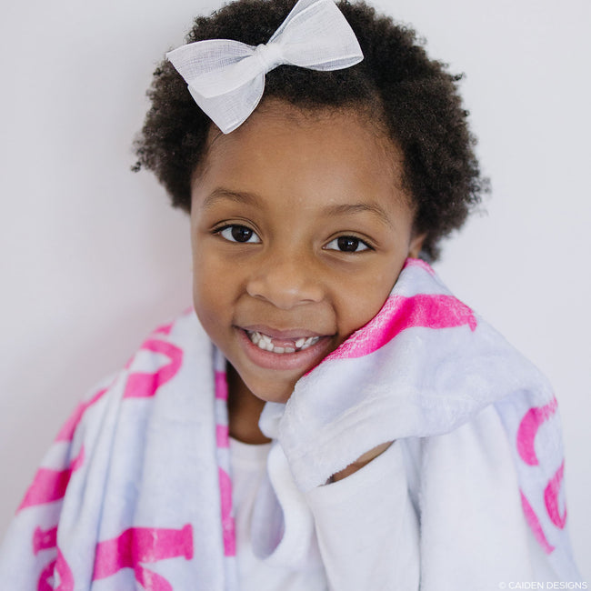 A child wrapped in a personalized blanket with hot pink names on it.