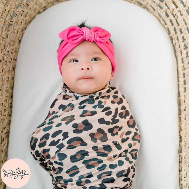 Close up of baby swaddled in brown leopard print baby swaddle and hot pink headband