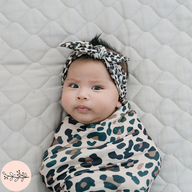 Close up of baby swaddled in brown leopard print baby swaddle and headband